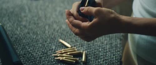 Woman Loading Bullets into Magazine on Grey Carpet