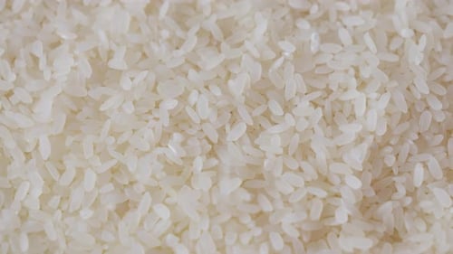 Clean Grains of polished white rice fall close up shot with black pebble spotted