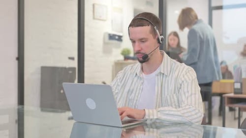 Creative Young Man with Headset Working on Laptop in Call Center