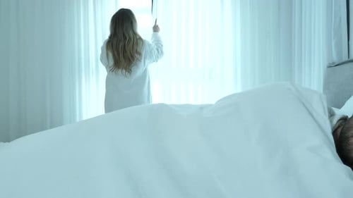 Woman Opens Curtains While Man Sleeps in Bedroom