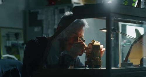 Man Repairs Clock with Magnifying Glass in Workshop