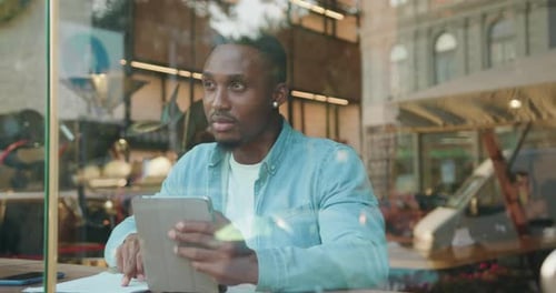 Young man checking documents with datas from tablet computer sitting in coffee shop
