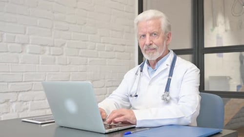 Senior Doctor Working on Laptop and Smiling