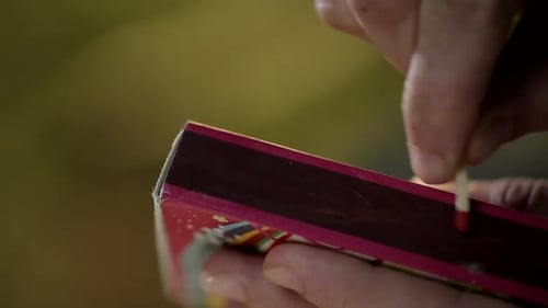 Close up of unidentified hand striking matchstick over matchbox to ignite it.