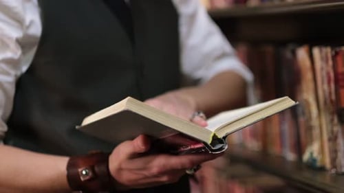Stylishly Dressed Man Leafing Through Vintage Books in an Old Dark Library Close Up View