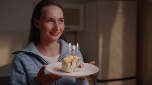 Garota encantadora em um suéter azul apaga velas em um bolo de aniversário A aniversariante é elegante