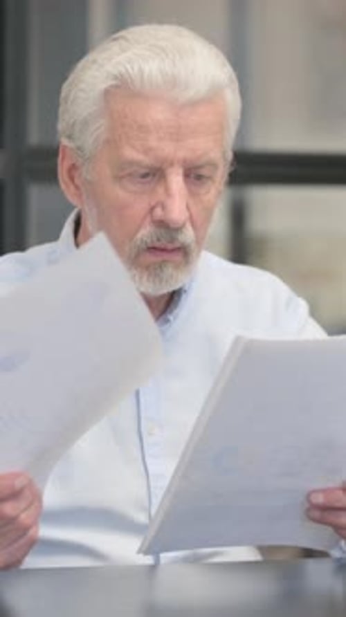 Senior Man Reads Document, Smiles, and Gives Thumbs Up