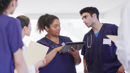 Video of diverse group of male and female doctors looking at tablet talking in hospital corridor