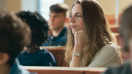 Schönes und intelligentes junges Mädchen hört einen Vortrag in einem Klassenzimmer voller multiethnischer Studien