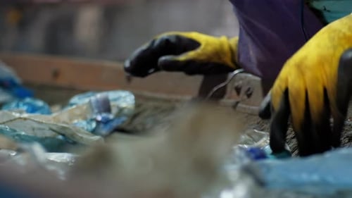 Worker in special wear sorting plastic garbage on a conveyor belt at waste recycling factory