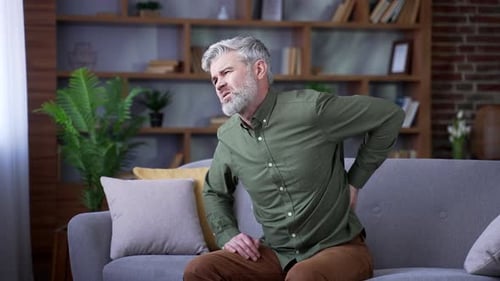 Man Sitting on Sofa Massaging Lower Back in Pain