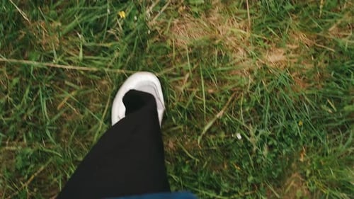 Pov View Frauenbeine in weißen Turnschuhen, die an der grünen Graswiese im Bergwald spazieren geht