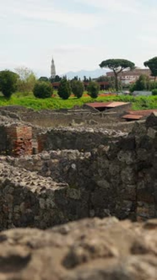Vertical view across Pompeii ruins with ancient stone walls in the foreground, green parkland,