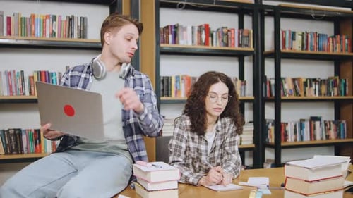 Étudiants collaborant dans un cadre de bibliothèque moderne tout en étudiant et en utilisant un ordinateur portable à une table en bois