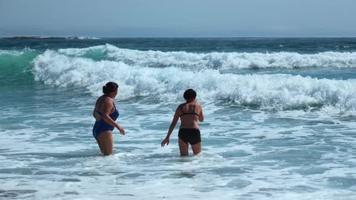 Women Wading into Ocean Waves on Sunny Day