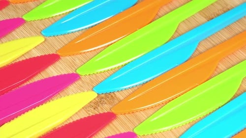 Bright Plastic Knives Arranged on Bamboo Board