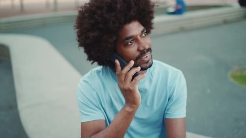 man sitting on city park bench and talking on smartphone