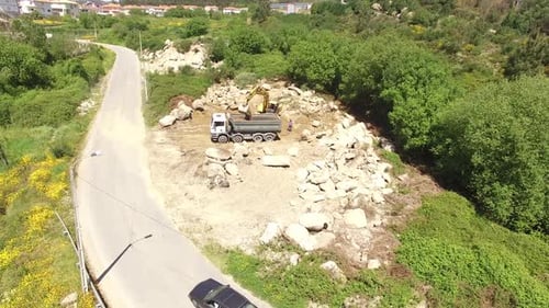 Aerial: Excavator Loading Truck with Rocks Next to Road