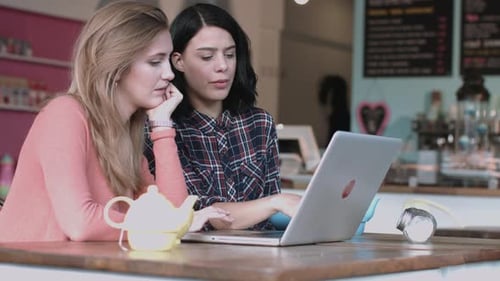 Dos mujeres adultas jóvenes que trabajan en un café con una computadora portátil