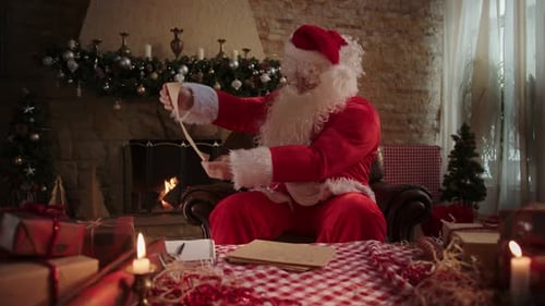 Santa Claus Reading Scroll by Fireplace at Christmas