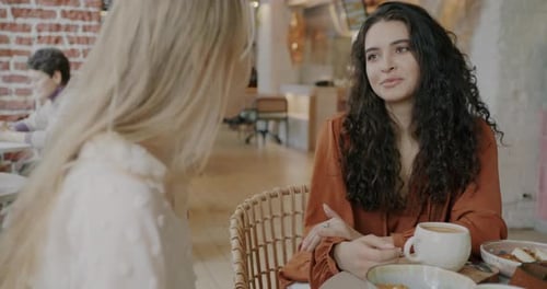Fröhliche junge Damen unterhalten sich und lächeln und genießen freundliche Gespräche im Café