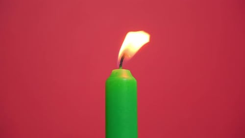 Close-up view of a single bright green candle burn on a red background.