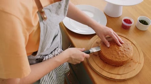 Woman cuts cake layer at wooden kitchen table
