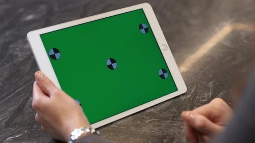 A business woman or manager holds a white tablet with a green screen. Close-up