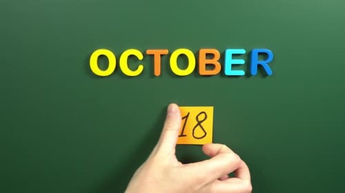 Hand sticking a sticker 18 October calendar day on school board. 18 date of October. Eighteenth