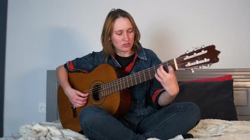 Woman Plays Acoustic Guitar While Sitting on Bed