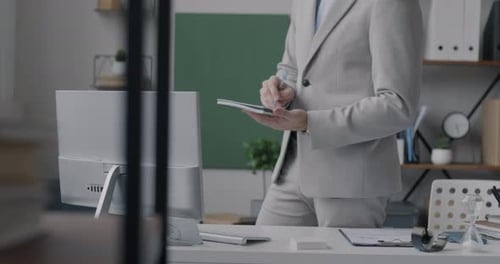 Low Shot of Businessman Writing in Notebook Standing in Office with Computer