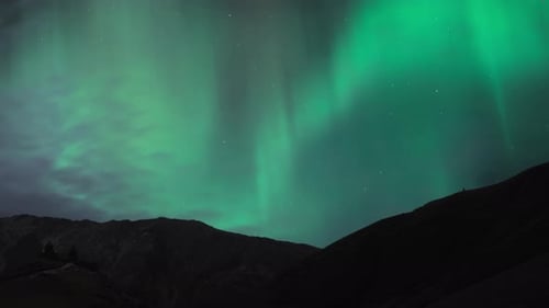 Aurora Borealis above mountains with clouds in the sky