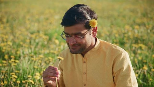 Young Man Smelling a Dandelion in a Field