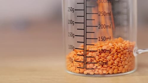 Red lentils pouring into glass storage jar in the kitchen close up, copy space. Nutritionology.