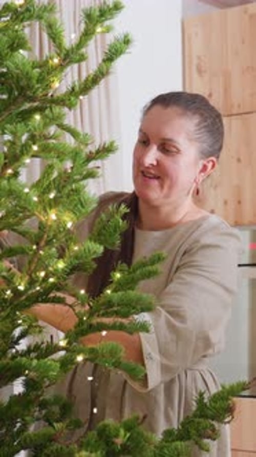 Woman Decorates Christmas Tree at Home with Lights