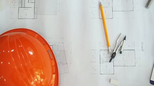 Top view shot of architectural helmet, pencil and dividers on architectural blueprints with panning