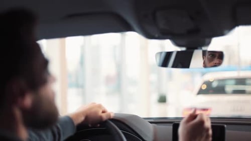 Man Sitting at Wheel of New Car Young Handsome Man with Beard Regulating and Looking at Rearview