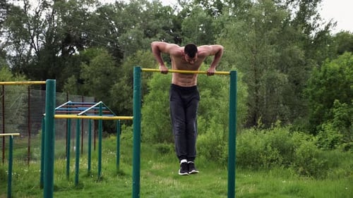 Starker und muskulöser Mann macht Übungen an der horizontalen Stange bei Nature Hardy Shirtless Sportsman