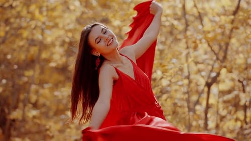 Beautiful Woman in a Red Dress Poses in a Bright Autumn Forest