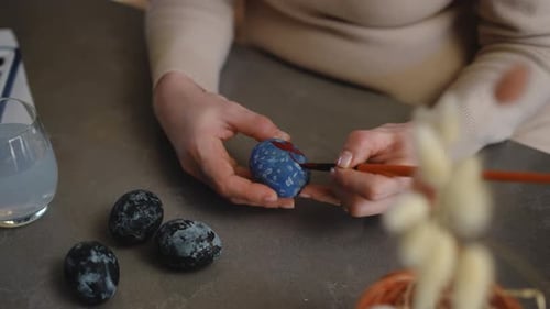 Closeup A Woman Ornaments an Easter Eggwhile Sitting at a Table in the Living Room Preparations for