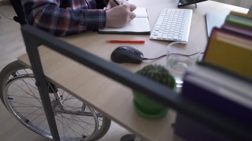 A Disabled Worker Sitting in a Wheelchair Works at a Computer