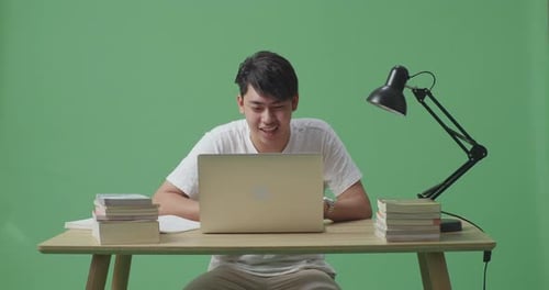 Young Asian Male Raising His Hand To Ask Question While Studying On A Laptop On Green Screen