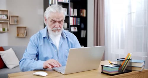 Senior Man Using Laptop at Desk in Bright Room