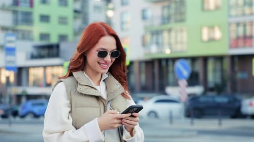 Smiling Caucasian Woman Walking on City Street and Using Smartphone Cheerful Female Texting While