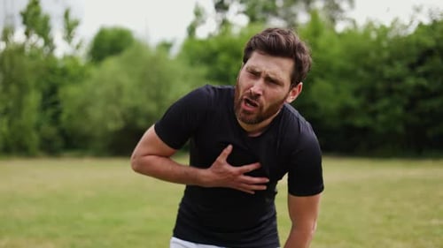 Erschöpfter Mann greift nach der Brust und fühlt sich schwer zu atmen, wenn er alleine steht