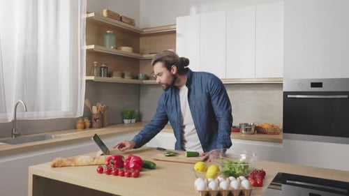 Man Checks Tablet While Prepping Food in Kitchen