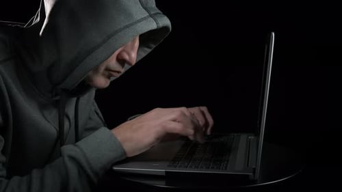 Man in Hooded Sweatshirt Typing on Laptop in Dark