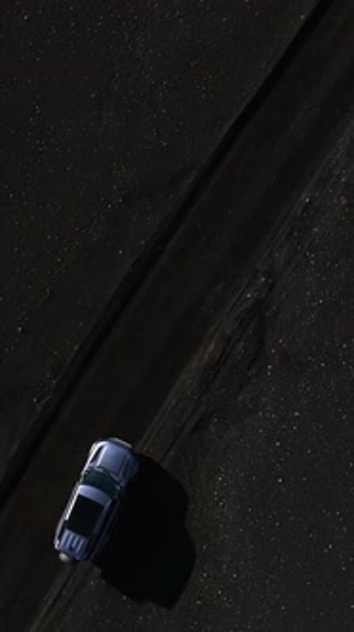 Top-down drone shot of an SUV starting to drive on a black volcanic sand track, leaving tire marks