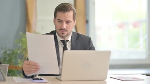 Man in Suit Reads Documents at Desk