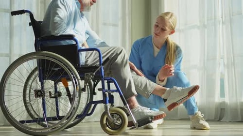 Senior Man in Wheelchair Receives Leg Therapy